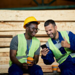 cheerful warehouse workers reading something funny on cell phone while having coffee break at work.